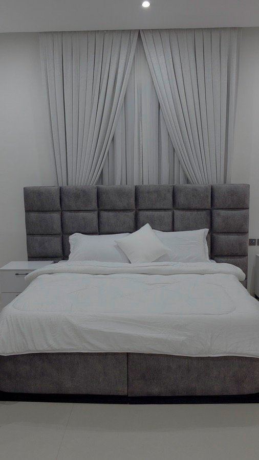 Completed bedroom with a tailored grey upholstered bed and bedside cabinets
